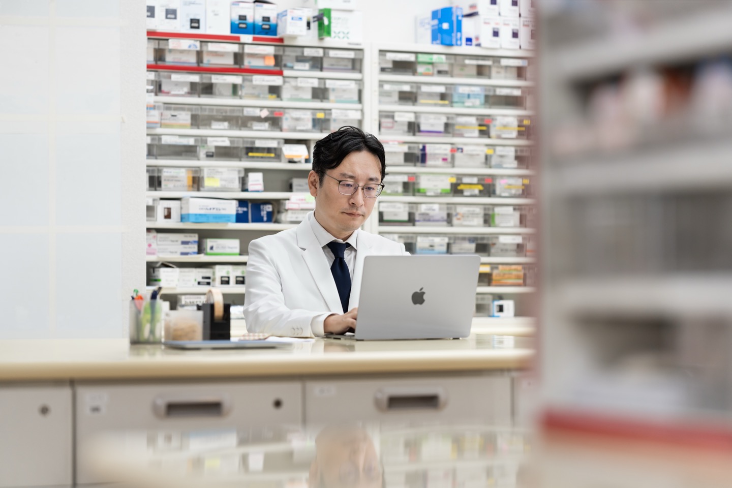 薬局内でMacを使い業務を確認する薬剤師